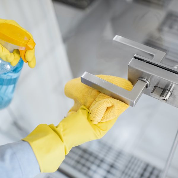 Woman in protective gloves disinfecting door handle while cleaning at home, close-up view on hands